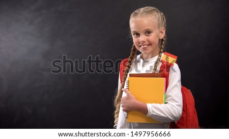Joyful pupil holding books with tiny Spain flag, ready to learn foreign language