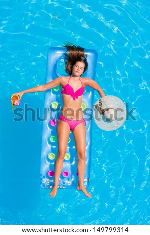 Young woman with straw hat and pineapple fresh cocktail on a lilo in the swimming pool