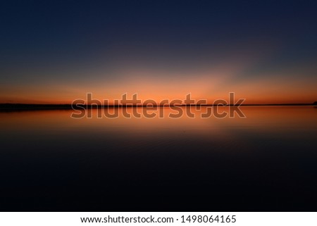 Bright blue sky in pink with a red twilight glow on the horizon over water