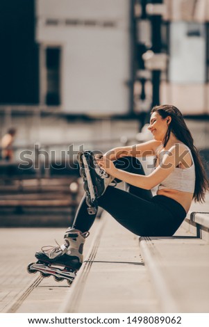 Beautiful girl resting after skating in the city and listening to music from her smartphone