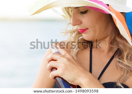A girl with a hat rubs a tanning cream over her shoulders.Alechi against the background of  blurred background of the sea. A woman of 30 years old in a beautiful bright summer hat puts on sun cream