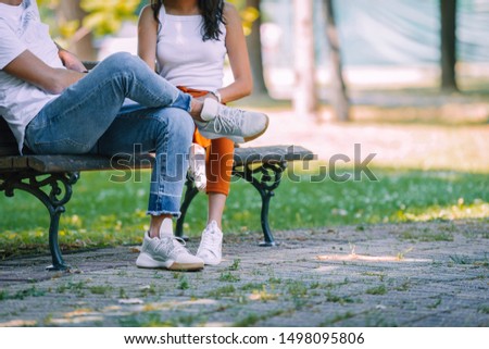 Stylish young couple in summer park happy and joyful sitting on a bench, unrecognizable faces