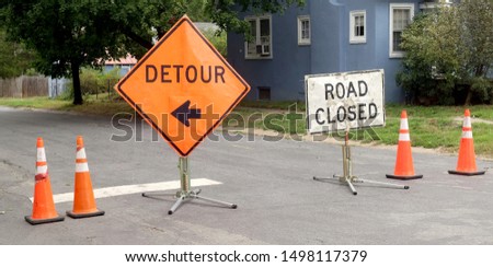 ROAD CLOSED and DETOUR signs flanked with orange safety cones in residential city neighborhood.