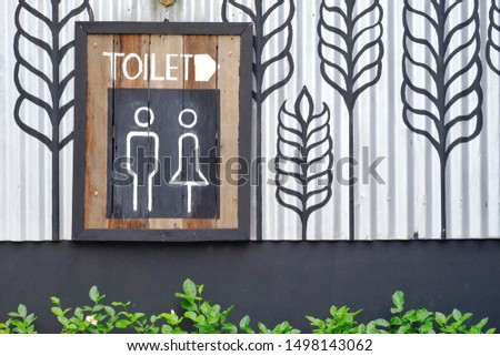A toilet sign with women and men icons  on wooden board and a white arrow and green leaves background