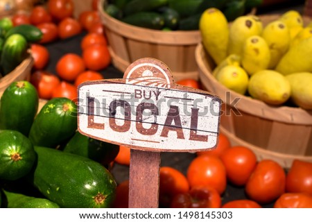 wooden sign with word signage reading buy local produce with tomatoes yellow squash and zucchini background