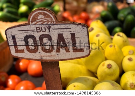 wooden sign with word signage reading buy local produce with tomatoes yellow squash and zucchini background