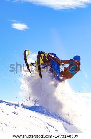 snowmobile jump. bright snowmobile in motion. the guy is flying on a snowmobile on a background of blue sky leaving a trail of splashes of white snow. 