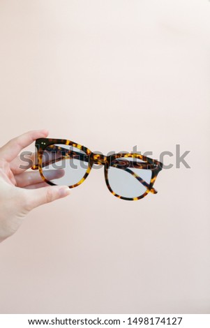 Woman holding tortoise shell blue light glasses in hand over pink background, copy space
