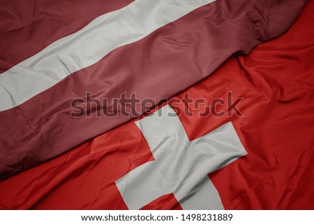 waving colorful flag of switzerland and national flag of latvia. macro