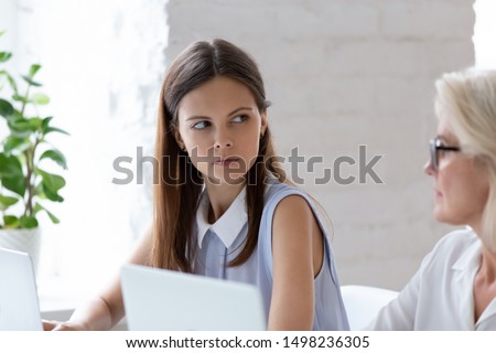 Serious millennial woman worker sit at office desk looking angry at senior colleague, grumpy young female employee feel mad dissatisfied having conflict or misunderstanding with coworker at workplace Royalty-Free Stock Photo #1498236305