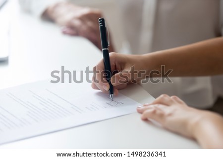 Close up of female job candidate hold pen put signature on official document in office, woman worker or applicant sign contract, close deal with business partner or client. Collaboration concept