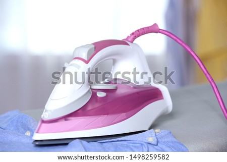 Modern electric iron and clean shirt on board indoors, closeup