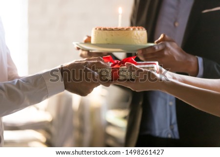 Close up employees congratulating colleague with birthday or promotion, giving gift box with bow and cake with candle, party in office, friendly workers making surprise, corporate celebration concept Royalty-Free Stock Photo #1498261427