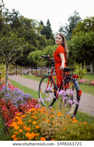 Beautiful girl in red dress near red retro bicycle in the park near flowers