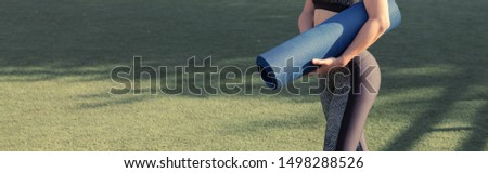 A young slim athletic girl in sportswear with snakeskin prints performs a set of exercises. Twists the yoga mat on the background of lawn grass. Panoramic image banner, toned.