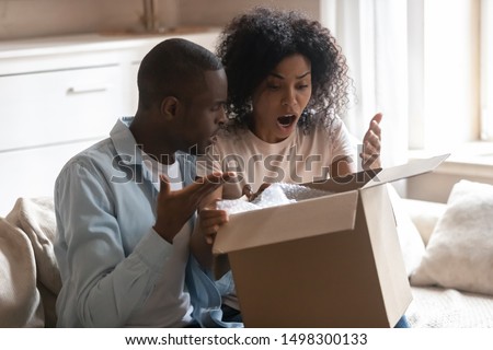 Disappointed biracial husband and wife unpack cardboard box get wrong order, frustrated african American client couple open unbox delivery package, feel confused receive bad quality, damaged product Royalty-Free Stock Photo #1498300133