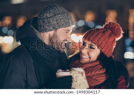 Photo of two overjoyed people with hot tea beverage in hands spending x-mas evening at decorated park wearing warm coats outside