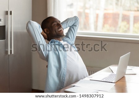 Calm relaxed african American male worker sit at table distracted from work dreaming or visualizing, peaceful dreamy biracial man lean back relax in chair with eyes closed smiling thinking of success Royalty-Free Stock Photo #1498307912