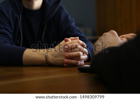 Police officer interrogating criminal in handcuffs at desk indoors Royalty-Free Stock Photo #1498309799