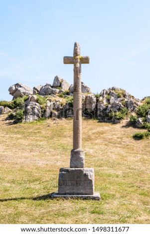 Eroded granite calvary of the chapel of Saint-Nicolas in Bugueles, Brittany, France, in front of a granite outcrop under a bright sunshine.