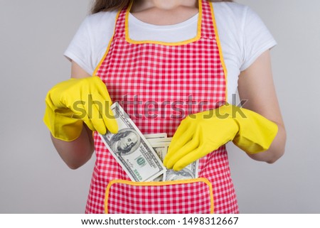 Professional people earn more concept. Cropped close up photo of satisfied happy confident lady putting money into pocket on her red apron isolated grey background