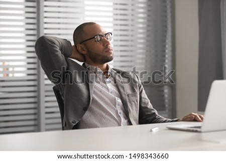 Tired upset stressed african american businessman in eyeglasses overload with computer work, holding head in hand, trying to relax, leaning on comfortable chair in office, looking at computer monitor.