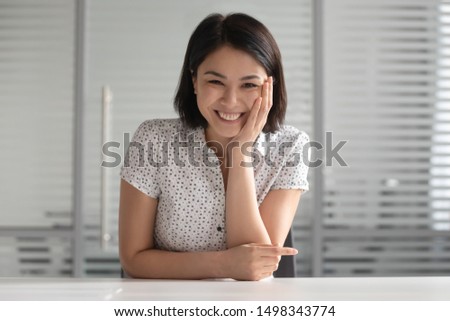 Happy asian woman sitting at table, looking at camera, having video call with friend or client, listening speaker, laughing at joke. Positive young female hr manager holding distant job interview. Royalty-Free Stock Photo #1498343774
