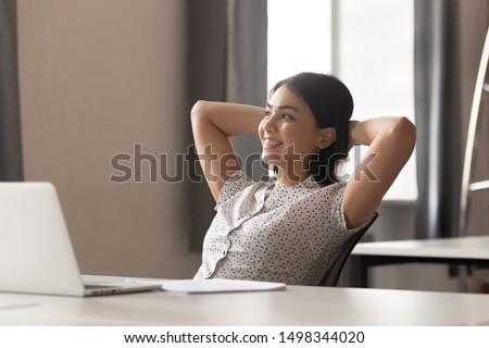 Happy peaceful asian female employee lean on comfortable office chair, holding hands behind head, relaxing during working day break or after completed job, looking aside, dreaming about vacation. Royalty-Free Stock Photo #1498344020