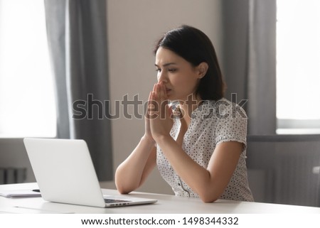 Sad worried asian female employee looking at laptop screen at office. Stressed upset manager stuck with hard task, thinking about correct difficult decision or hard problem solution, hoping for help.