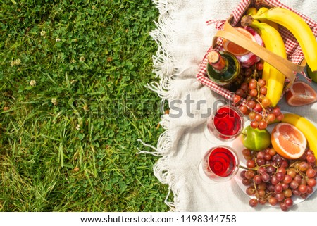 Flat lay Picnic on a green lawn, with a plaid fruit and picnic basket and a bottle of wine and glasses with red wine, with space. Summer mood and outdoor recreation