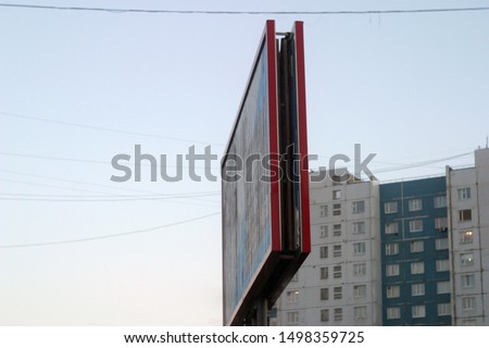 Billboard of bright red color a look with a side on the city street against the background of the blue and White multi-storey building with square windows and the gray sky, electric wires.