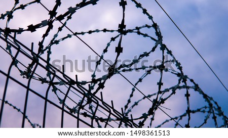 The fence of the correctional facility with barbed wire on the background of a gloomy cloudy dark blue sky. Royalty-Free Stock Photo #1498361513
