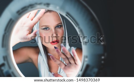 Attractive young blonde in a holographic silver bodysuit looks like in the porthole of a spaceship. Futuristic portrait.