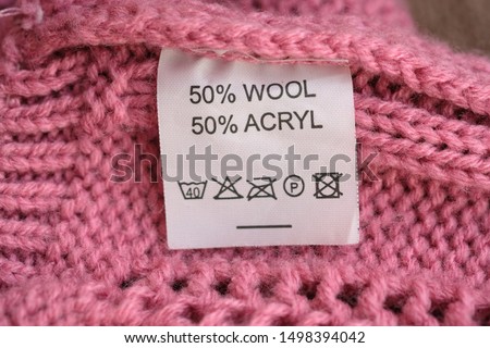 Wrong side of a pink knitted sweater made of wool, the composition is specified: 50% wool and 50% acryl. Fabric composition white clothes label on pink texture background.