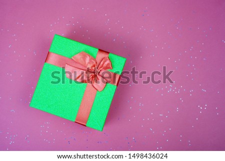 Green gift box with a red bow on a burgundy background with sparkles. View from above. Place for text.