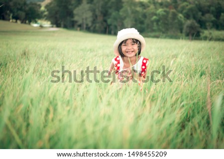 Happy kids playing on grass in meadow, cute children smiling and wearing hat, she sitting on pasture on blurred forest background