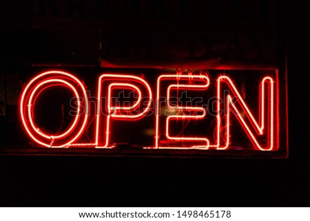 Neon sign with red lettering reading open from a store at night with a black background