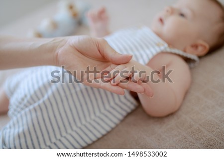 Close up of mom holding son's tiny hand. Baby lying on bed. Selective focus on hands.