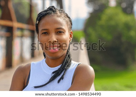 Thoughtful young African woman with a quiet smile and her braided hair across her shoulder looking intently at the camera outdoors on a rural bridge