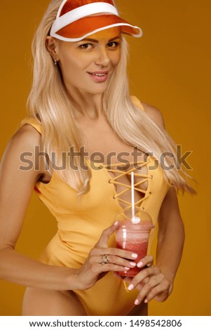 portrait of blonde girl in bathing suit and hat holding a fresh juice on orange background. healthy life