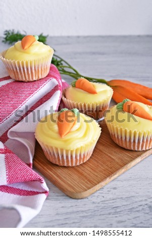 Freshly baked carrot muffins with cream cheese topping and a carrot of marzipan as decoration lie on a light wooden surface
