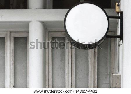 Photo of empty white circle space with classical outdoor light box for mock up display. Signage with shadow in white frame with exterior city wall background.