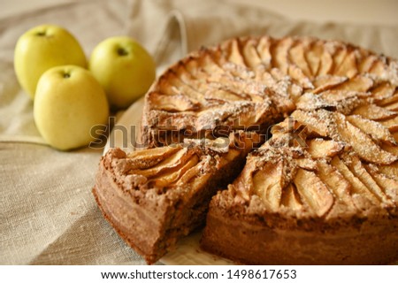 prepared apple pie charlotte on a linen gray tablecloth on a white table near three homemade green apples Royalty-Free Stock Photo #1498617653