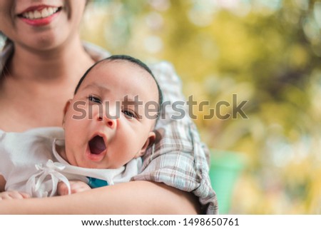 Young asian woman holding a newborn baby in her arms, baby yawning, Selective focus.