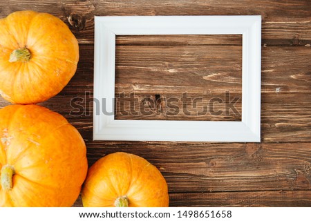 Pumpkins with white frame for picture over wooden background. Thanksgiving and Halloween concept. View from above. Top view. Copy space for text and design
