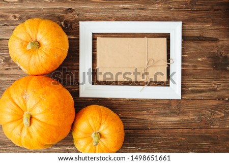 Pumpkins with white frame for picture and brown paper package tied up with strings inside over wooden background. Thanksgiving and Halloween concept. View from above.