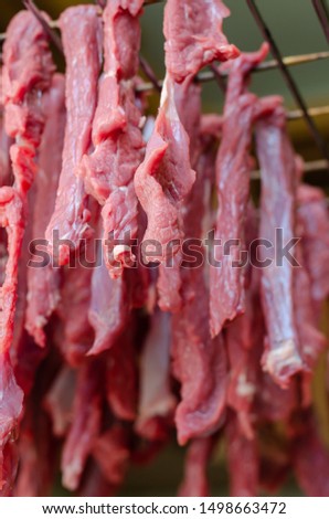Sliced narrow pieces of raw beef without salt and spices hang on a wire rack for drying. Cooking Dried Jerk. Shooting from the bottom up. Soft focus. Close-up. Vertical version of the photo.
