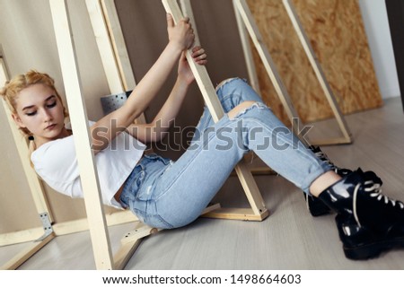 Female model is posing on the floor, in white shirt, denim jeans with holes and big black shoes. Fashion photo shoot. Photo studio backstage.