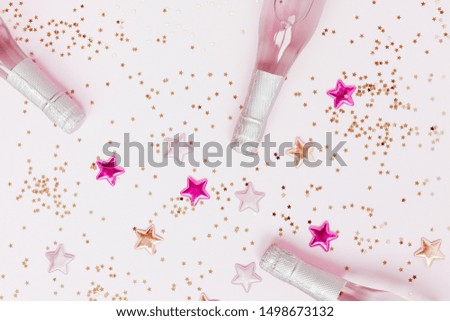 Christmas or New Year composition with bottles of rose champagne and golden shiny sparkle star confetti on pastel pink background, top view. Celebration flat lay. Party creative concept