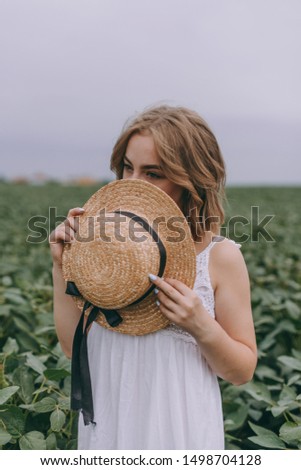 beautiful girl covers her face with a hat. Attractive young woman in a white bohemian dress with windy hair continues to relax among the leaves. summer vacation